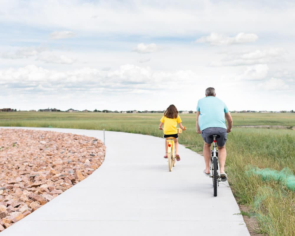 A father and daughter biking together on a spacious bike trail.